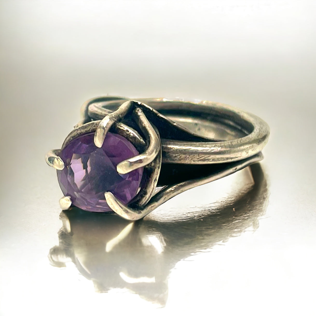 a sterling silver and amethyst ring rests on a white reflective tabletop surface