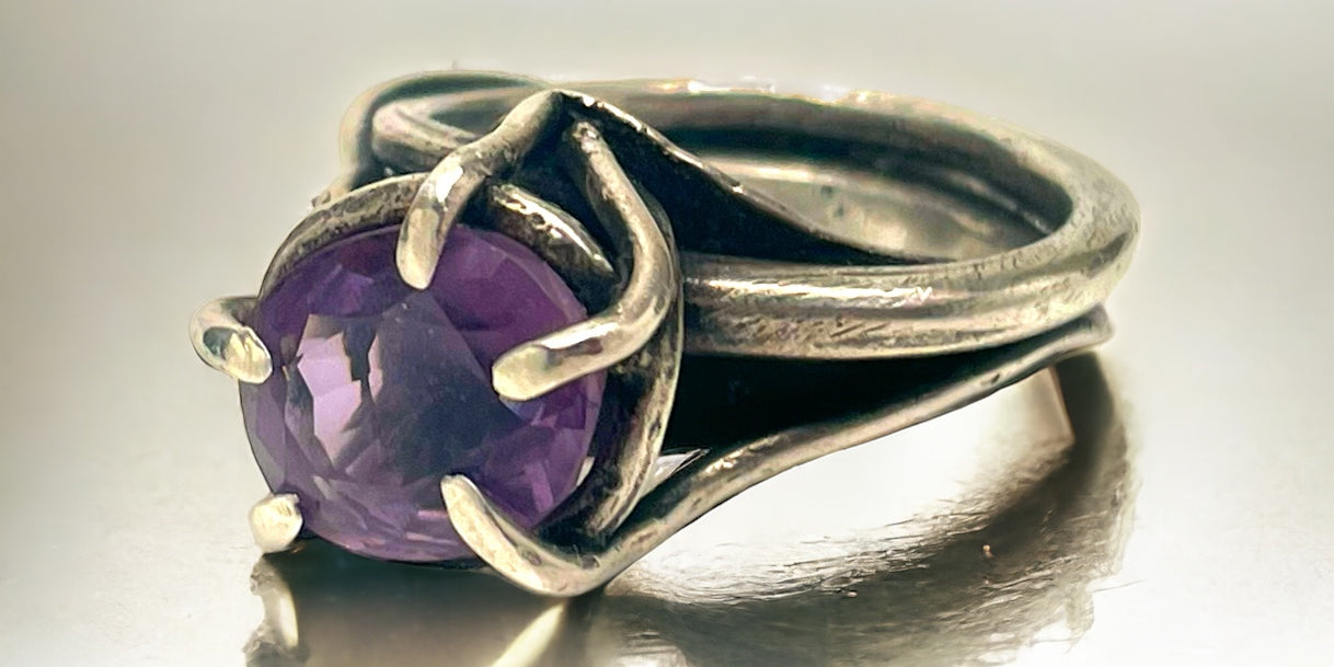 a sterling silver and amethyst ring rests on a white reflective tabletop surface
